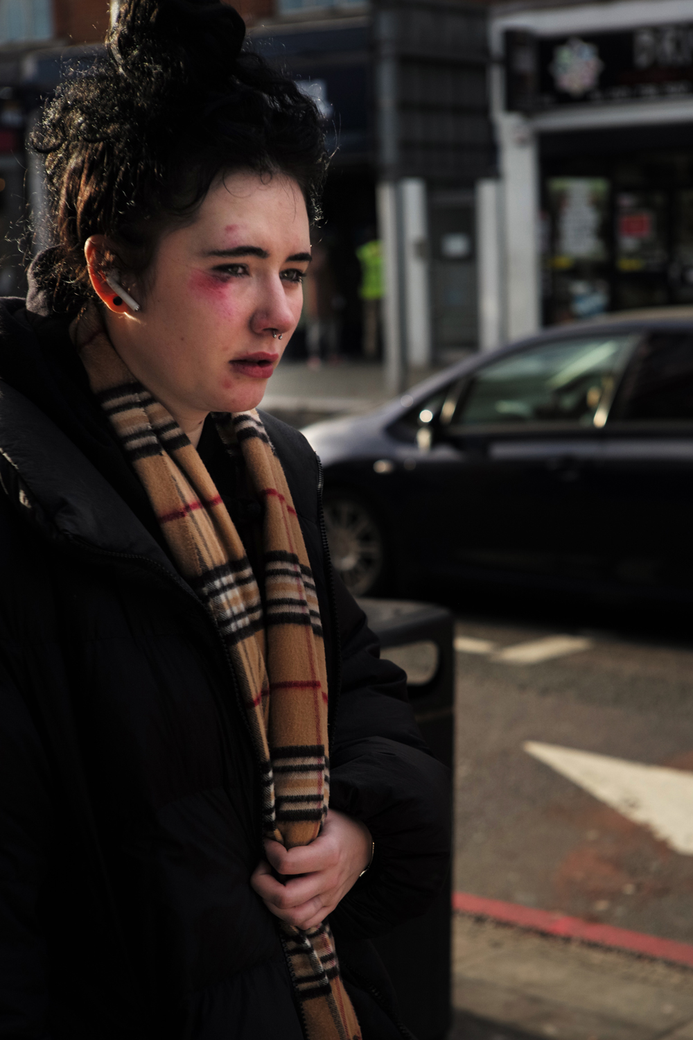 Woman in a tartan scarf caught in hard winter sun, London bus stop
