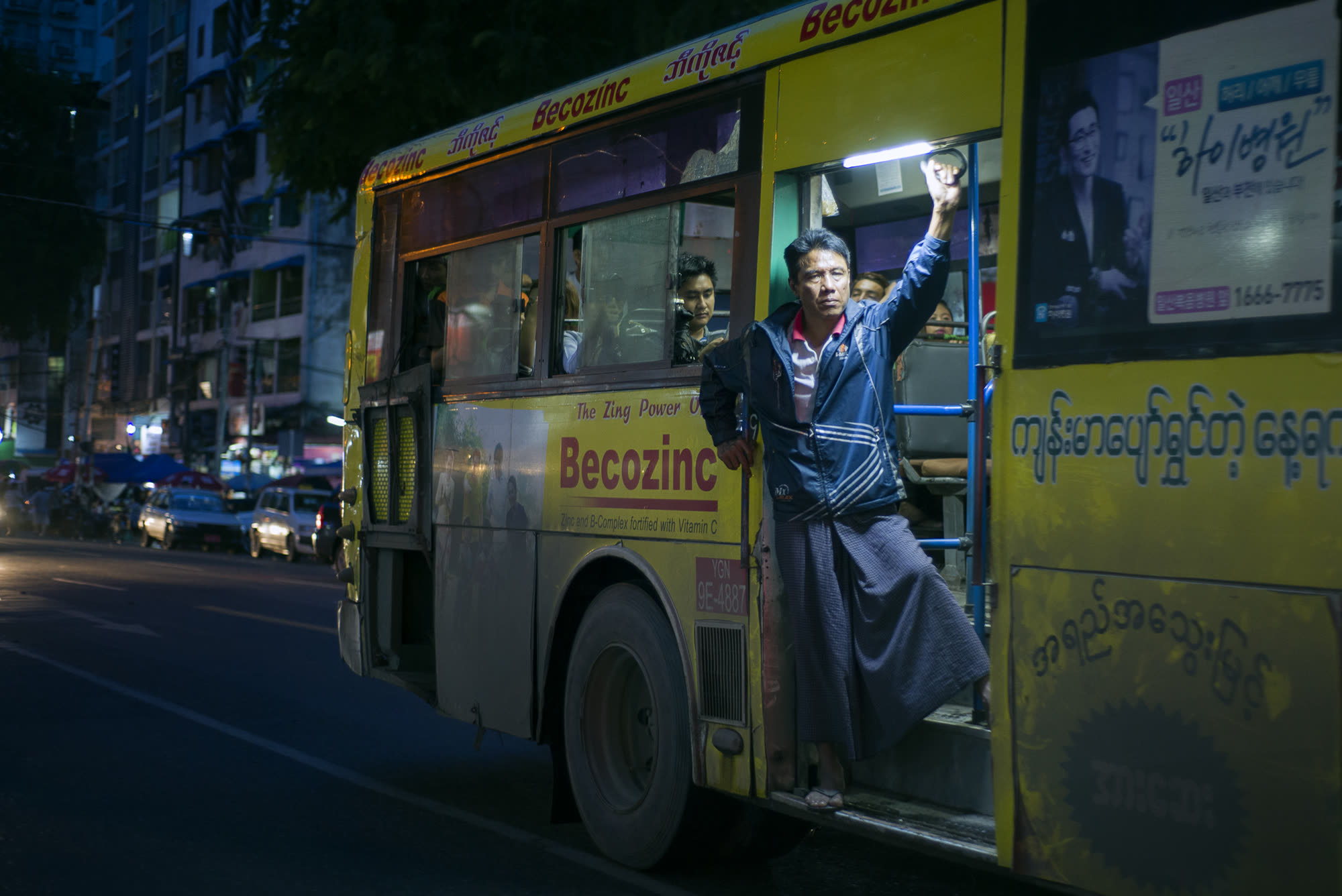 A conductor riding the open door of a Yangon bus